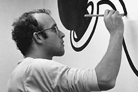 Keith Haring terwijl hij op 14 maart 1986 in het Stedelijk Museum in Amsterdam werkt aan een muurschildering.